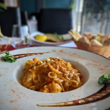 Bowl of pasta with king prawns in tomato sauce, bread basket behind